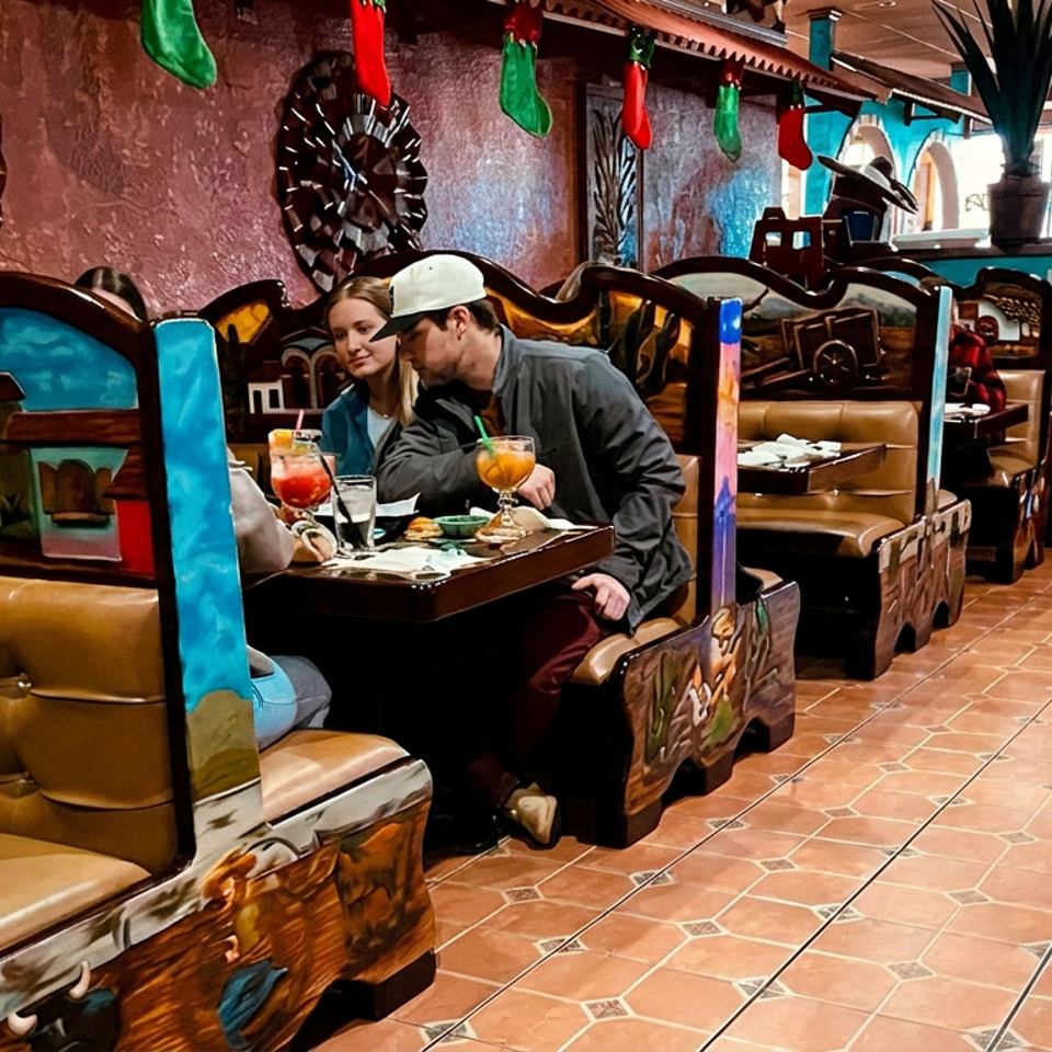 Diners enjoy drinks in colorful western-themed restaurant booths decorated with cowboy art, wagon wheels, and sombreros.